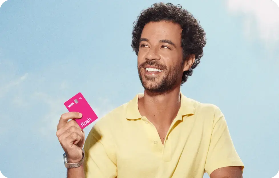 Homem sorrindo segura o cartão multibenefícios da Flash em um ambiente externo com céu azul.